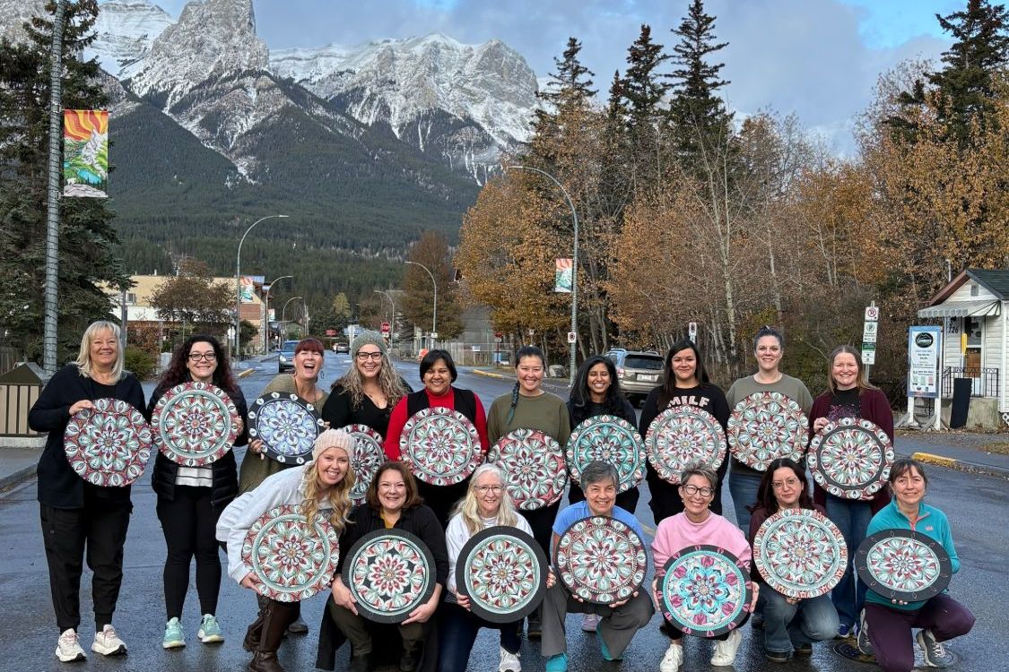 Lauren with a group of students, each holding their finished mandala, in front of the mountains in Canmore, Alberta